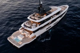 Dramatic aerial stern view of Cada Dia at dusk, revealing her illuminated decks, spacious outdoor lounges, and stunning aft beach club over open water.