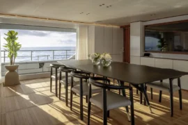 Elegant dining area aboard Cada Dia featuring warm natural light, modern furnishings, and seamless access to ocean views through expansive windows.